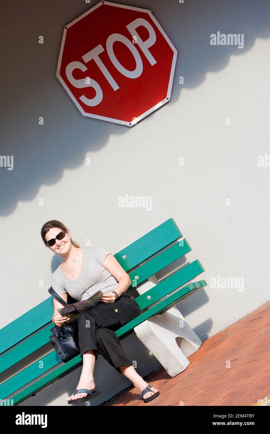Mid adult woman sitting on a bench and smiling Stock Photo