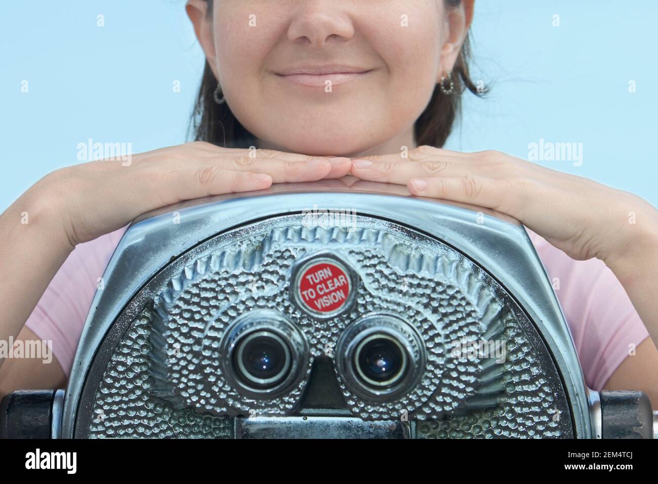 Mid section view of a mid adult woman resting her chin on a pair of coin-operated binoculars and smiling Stock Photo