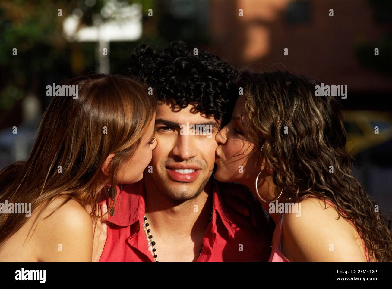 Portrait of two young women kissing a young man Stock Photo