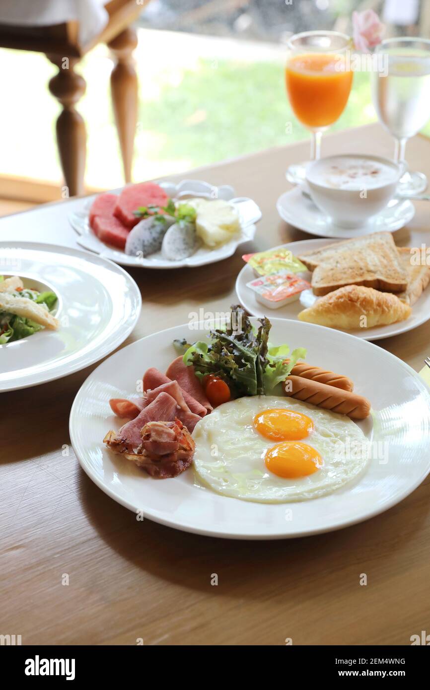 Breakfast set with fried eggs, bacon, sausages, beans, toasts, fresh salad and fruit on wood table Stock Photo