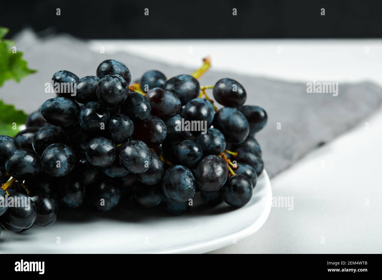 Black grape with leaf on white plate with grey tablecloth Stock Photo ...