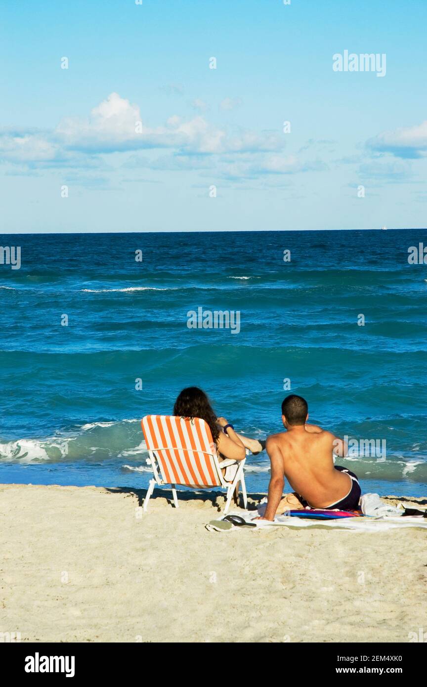 Rear view of a man and a woman sitting on the beach, Miami, Florida ...