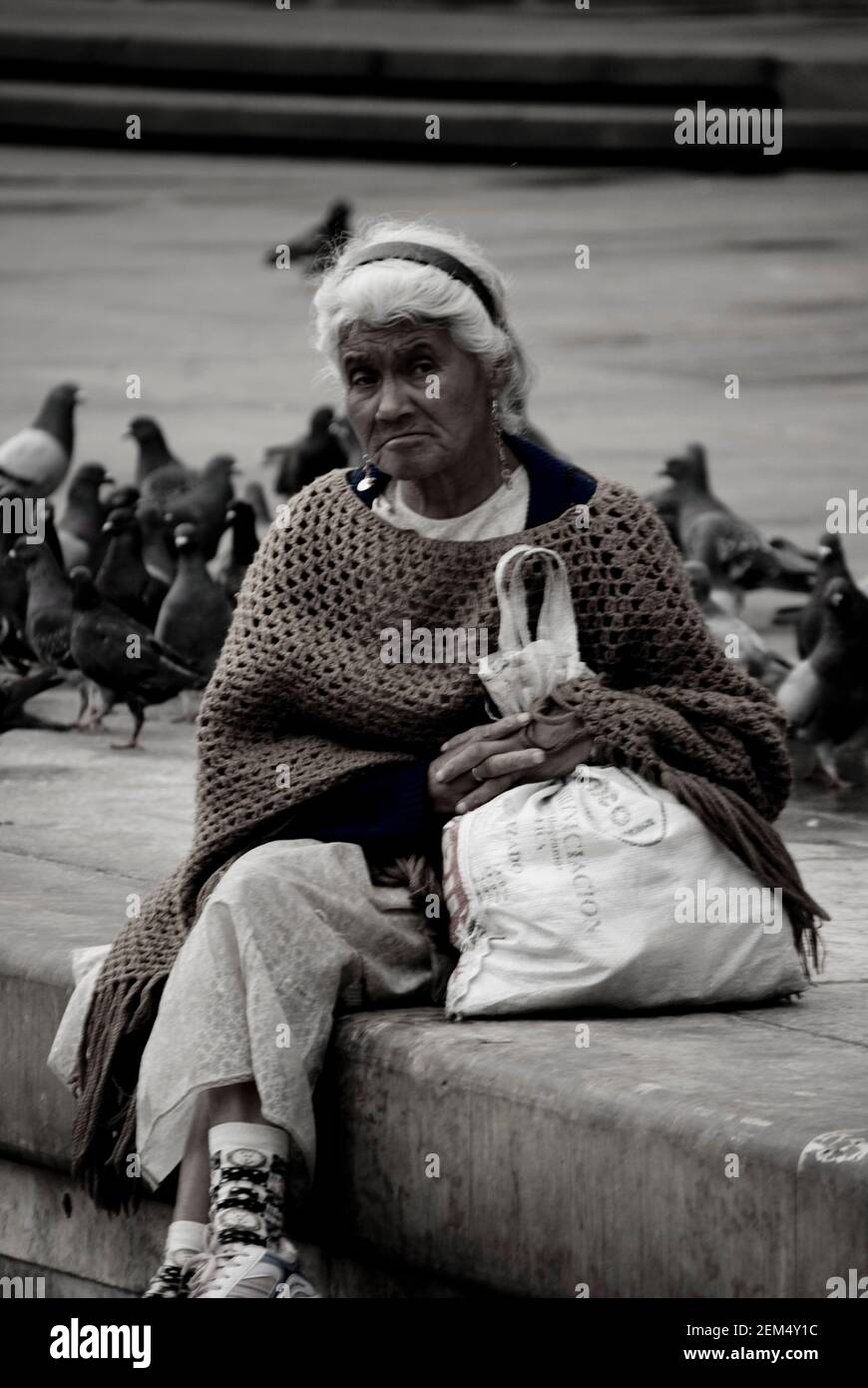 Senior woman sitting with flock of pigeons in the background Stock Photo