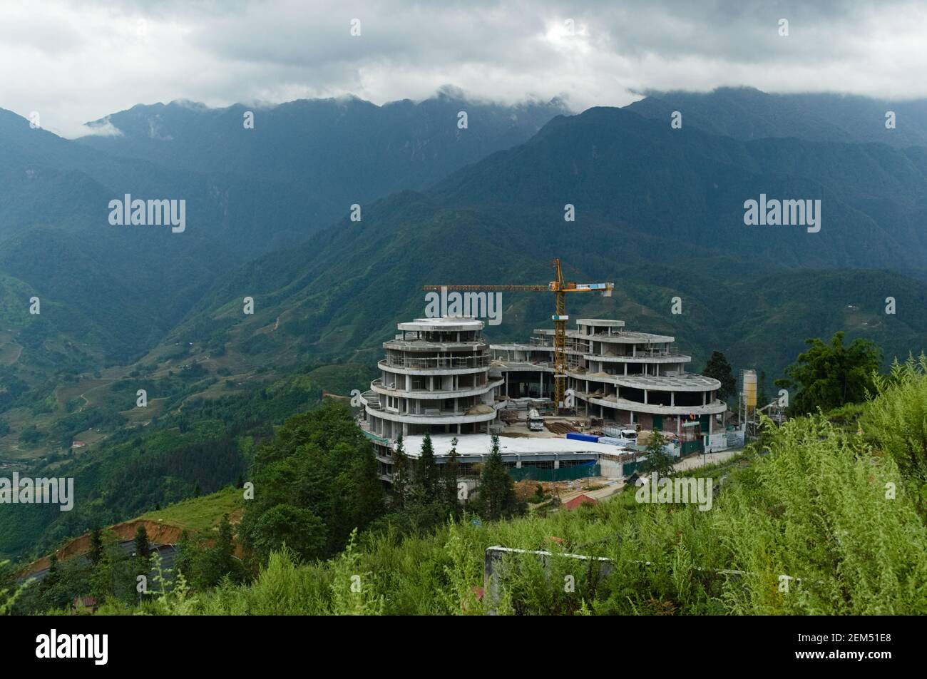 Construction site with crane. Building activity on the hill on background of mountain range. Stunning landscape with terraces near Sa Pa city. Vietnam Stock Photo
