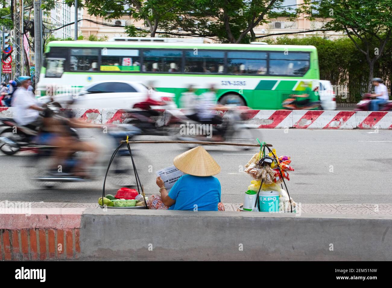July, 2015 - Ho Chi Minh, Vietnam: Vietnamese woman selling street food along the road with driving traffic in motion. Stock Photo