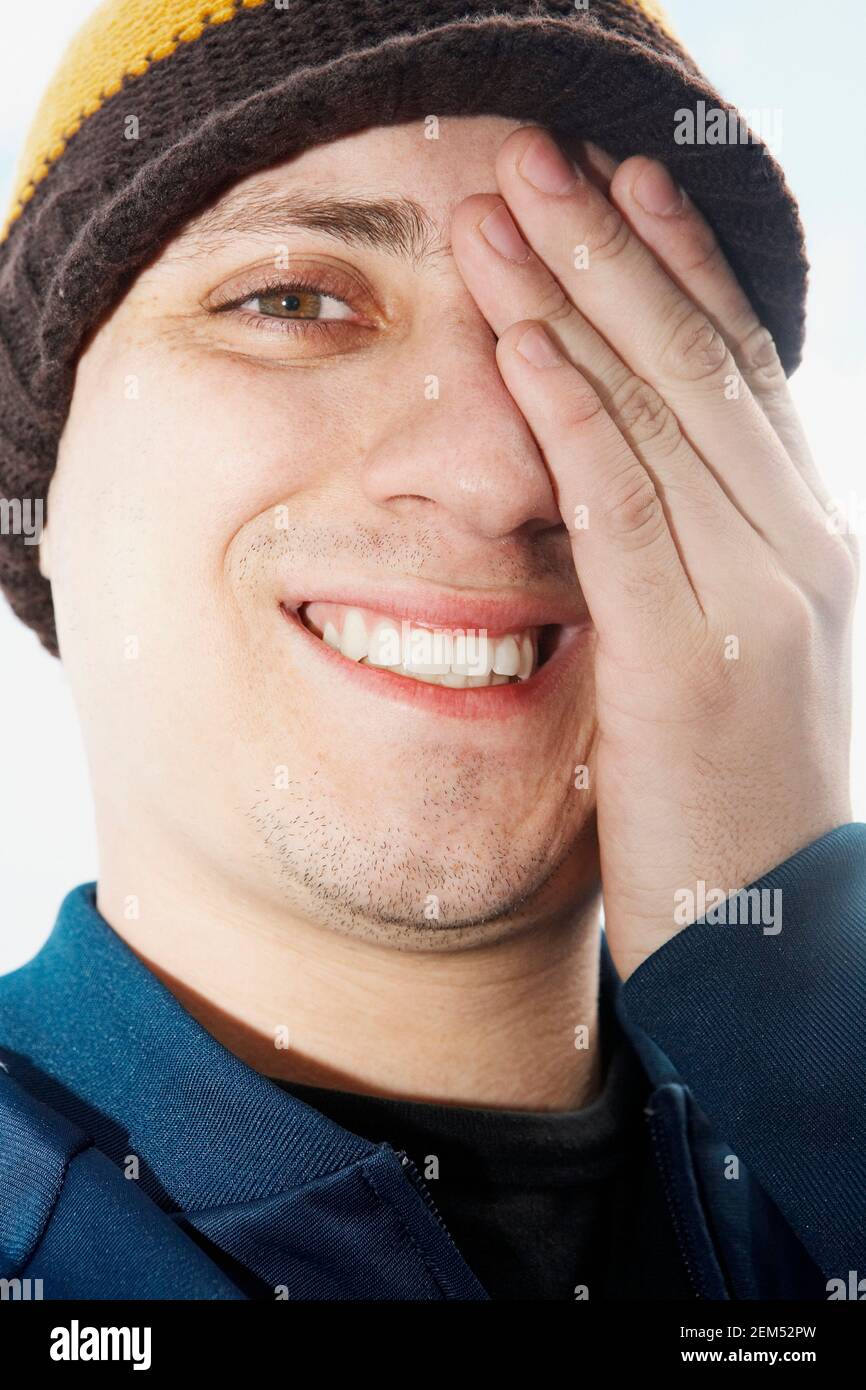 Portrait of a young man covering his eye with his hand and smiling ...