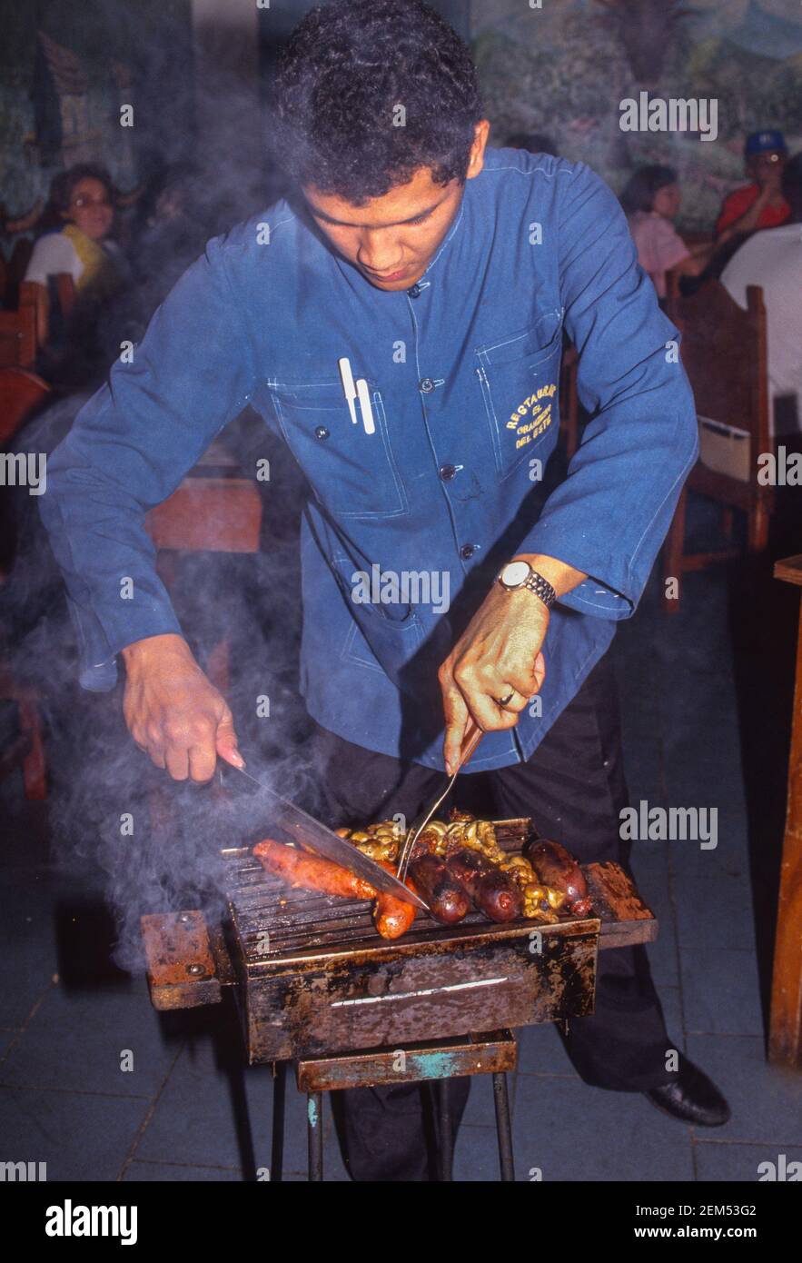 CARACAS, VENEZUELA, 1988 - Server carves grilled meat at table in El Granjero del Este restaurant. Meat a la parrilla. Stock Photo