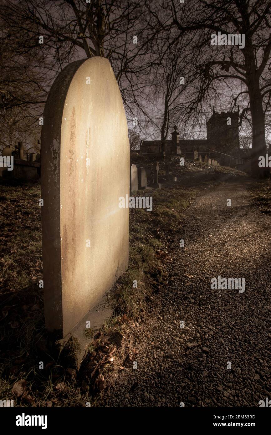 Blank headstone in a country churchyard lit by the sun's rays Stock Photo