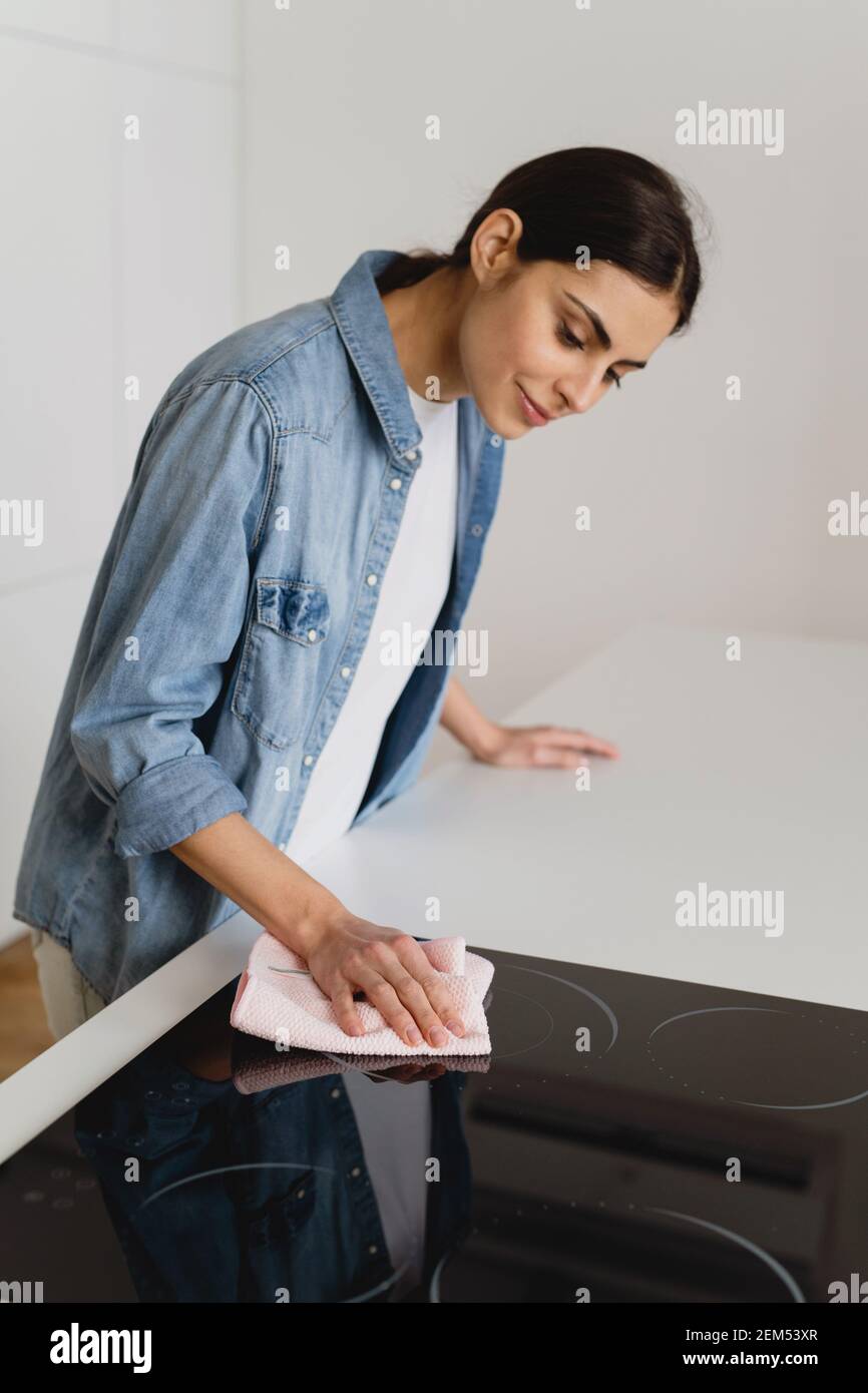 Young woman cleaning induction stove at home. Stock Photo