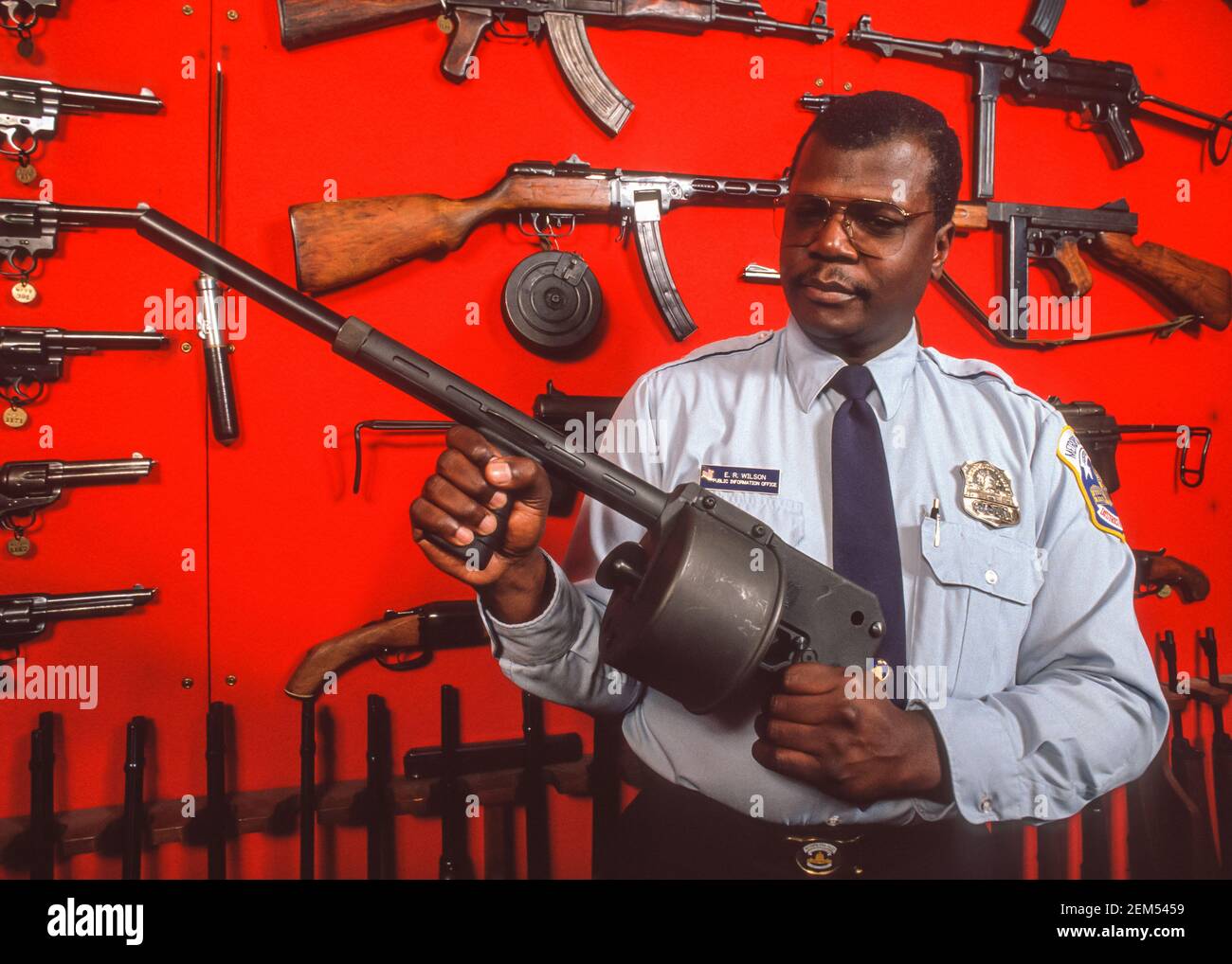 WASHINGTON, DC, USA - Police officer holds gun in front of display of confiscated guns, seized on streets by DC's Metropolitan Police Department, MPD. Stock Photo