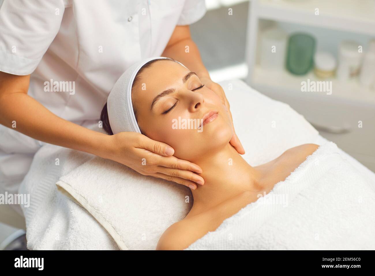 Hands of cosmetologist making manual relaxing rejuvenating facial massage for young woman Stock Photo