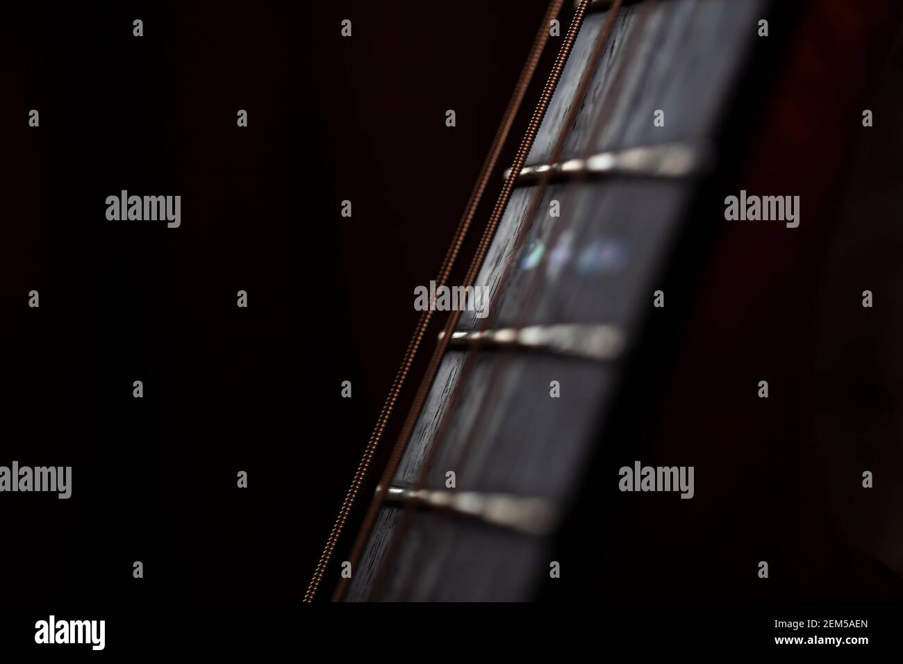 Close up of a steel strung guitars rosewood fretboard or fingerboard.Shot against a dark background.The strings are the phosphor bronze type. Stock Photo