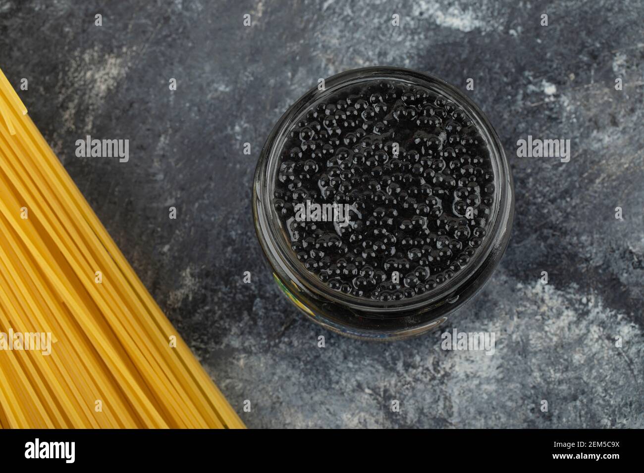 A glass plate of black sturgeon caviar with uncooked pasta Stock Photo