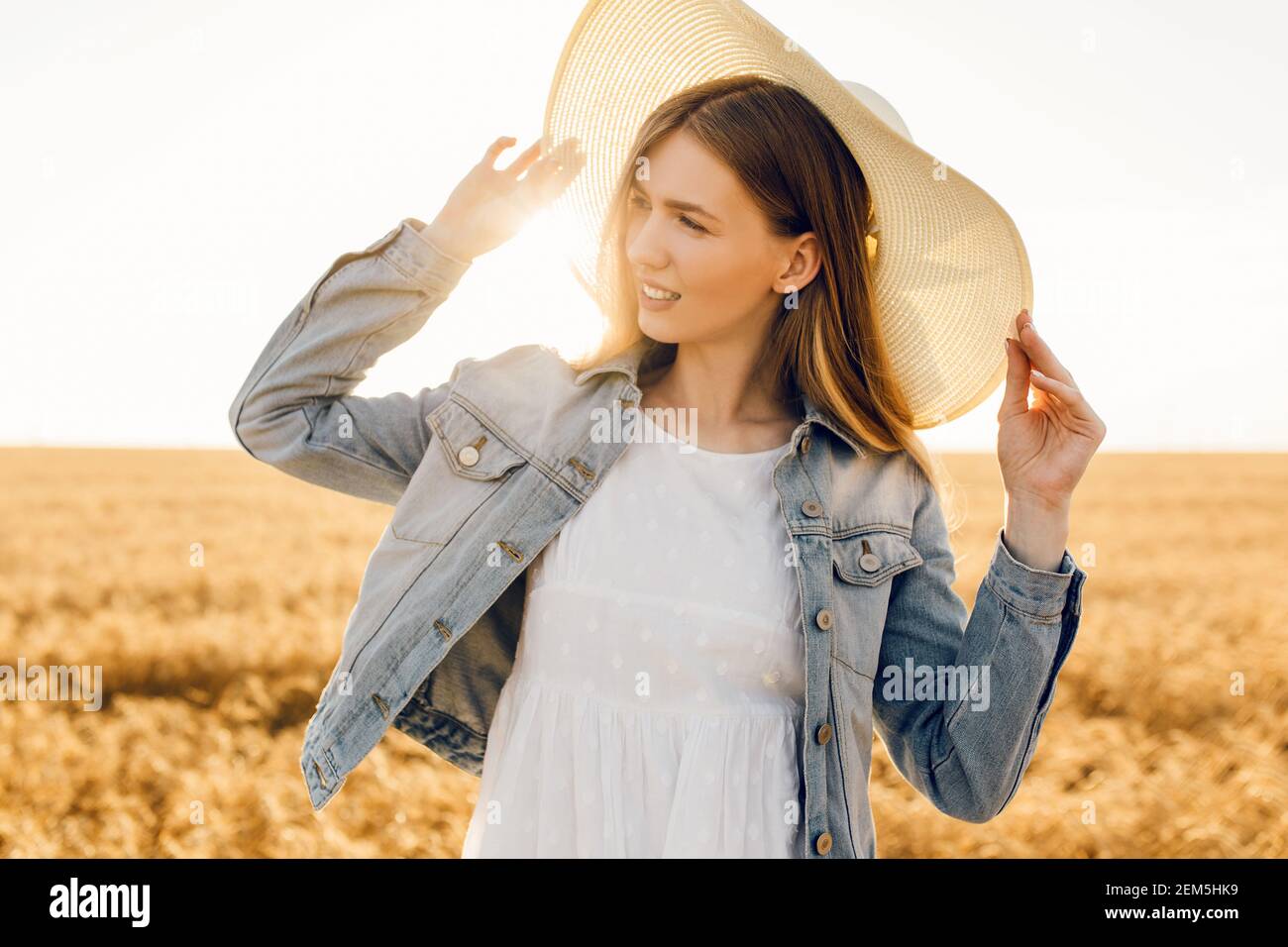 Happy beautiful young woman in dress and hat in a wheat field at sunset ...