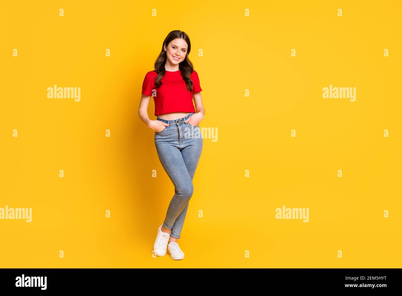 Full size photo of attractive lady standing arms pockets wear casual red cropped top jeans isolated yellow color background Stock Photo