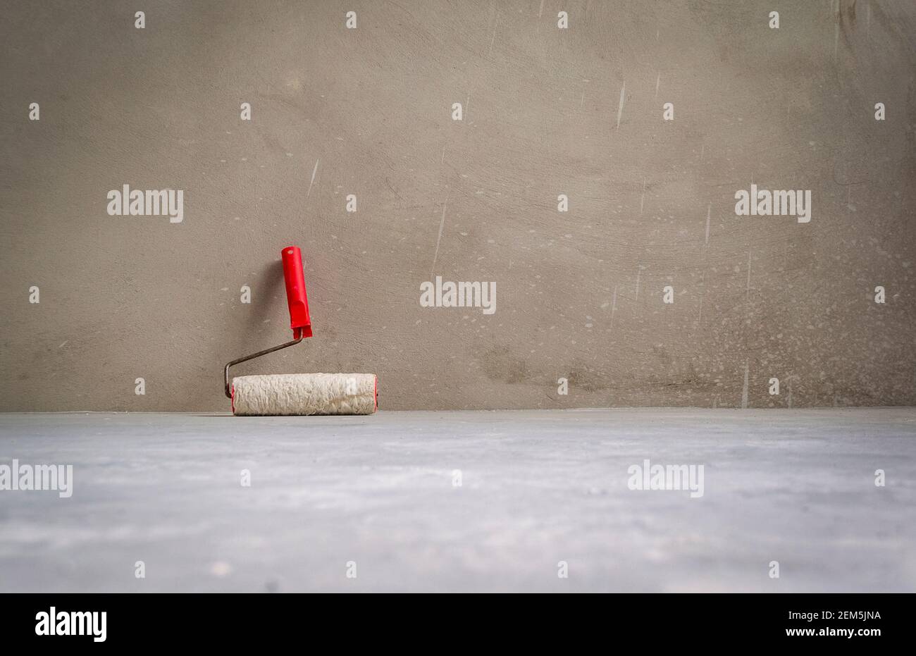 Paint roller in empty room on cement floor. Grunge interior background. Stock Photo