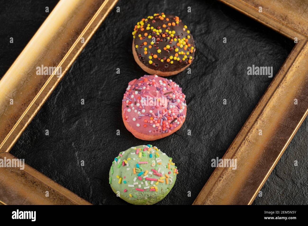 Sweet small doughnuts with sprinkles on a black background Stock Photo