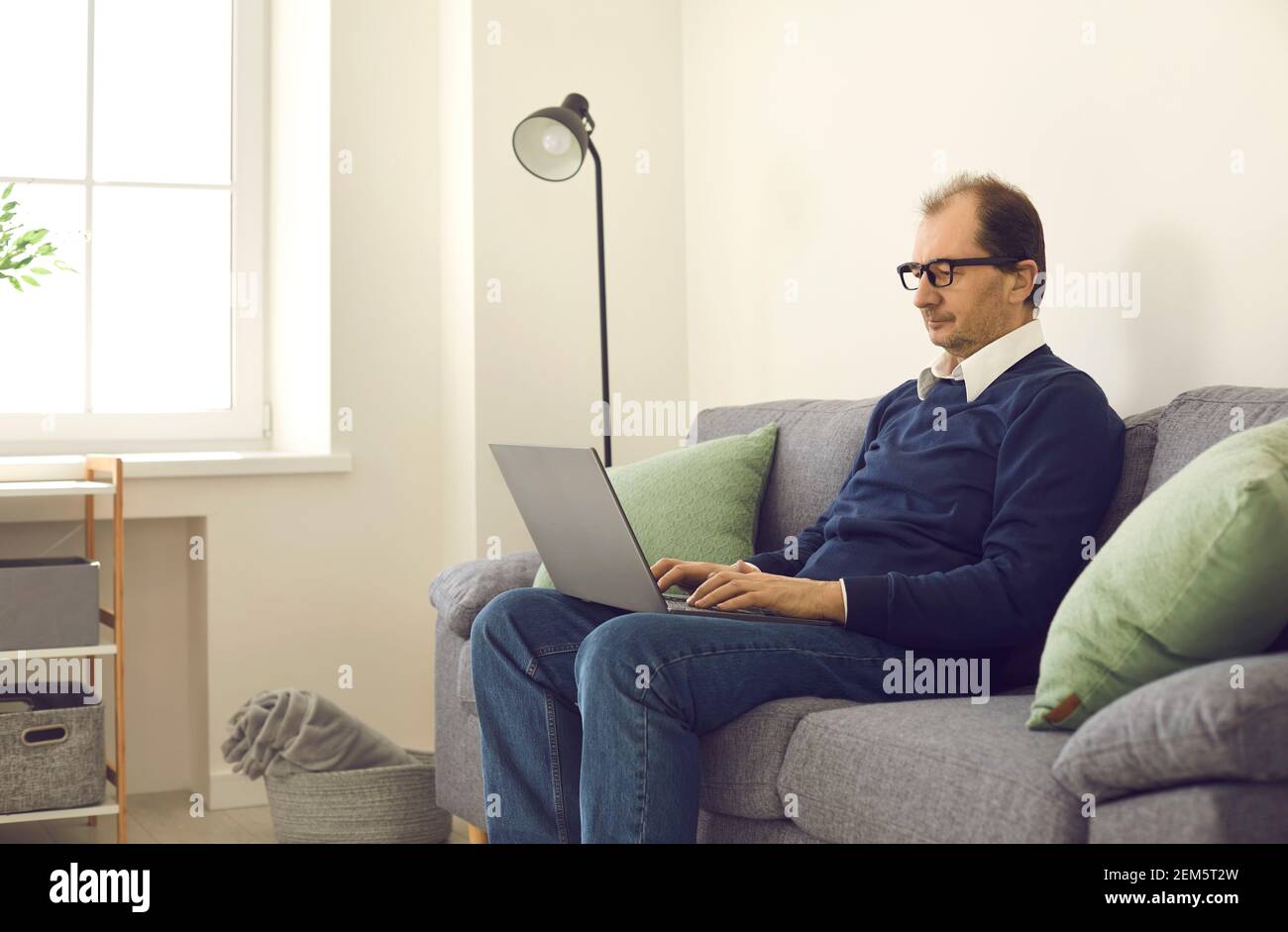 Mature remote worker using his laptop while sitting on comfortable couch at home Stock Photo