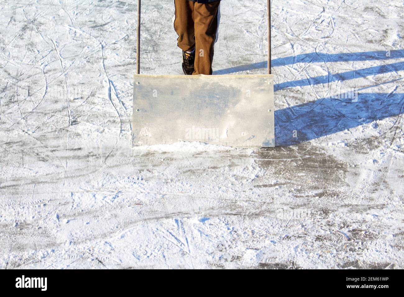 Toddler boy cleaning snow with special shovel on nature ice rink in the