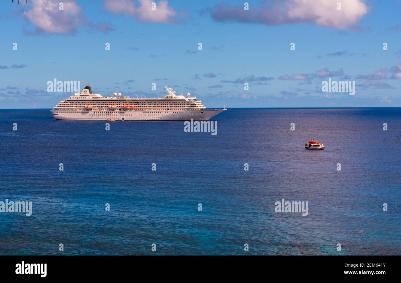 Niue, South Pacific -- March 12, 2018. Photo of a luxury cruise ship at sea in the South Pacific; a small tender craft makes  its way to  the island o Stock Photo