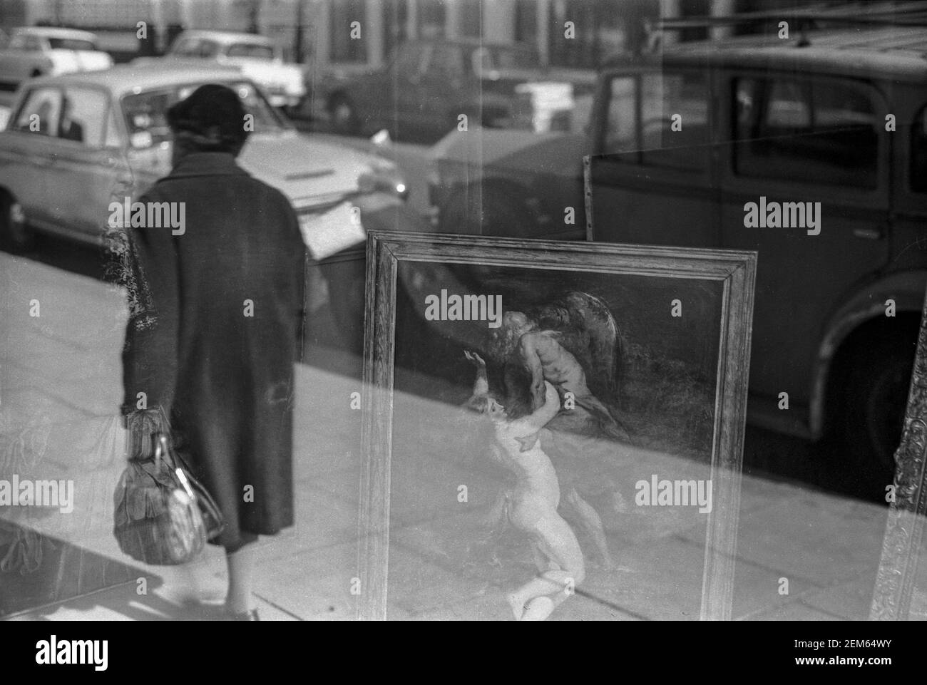 UK, West London, Notting Hill, 1973. Reflections in a shop window selling antiques & paintings. Outside is parked an old, antique car. Stock Photo
