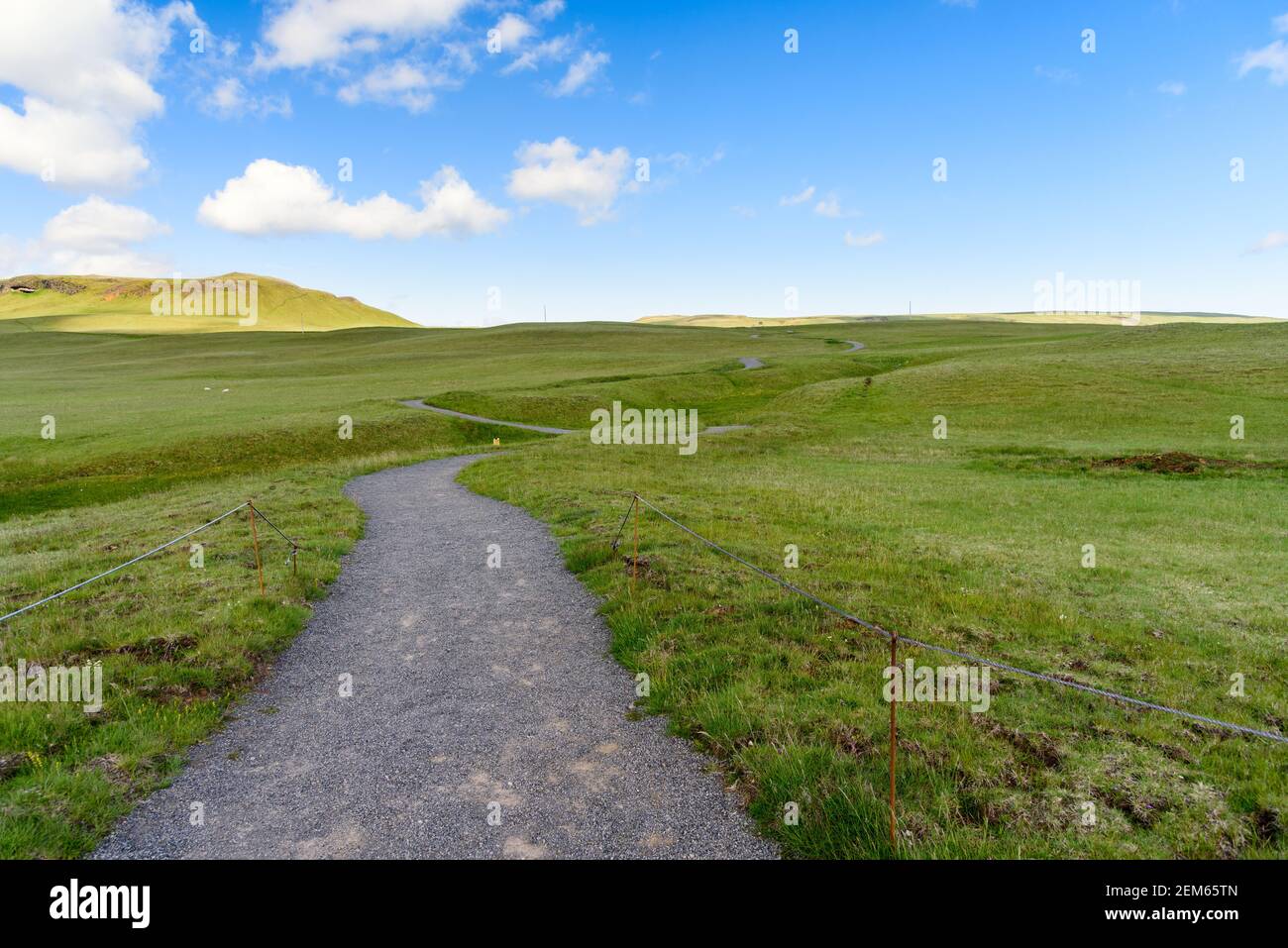 Deserted winding gravel path running through a meadow on a sunny summer day. Concept of solitude. Stock Photo