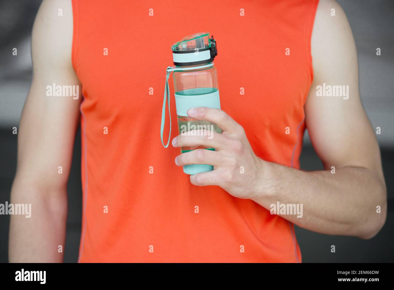 Hand holds sportive bottle of water or sport drink, male body background. Bottle of water in