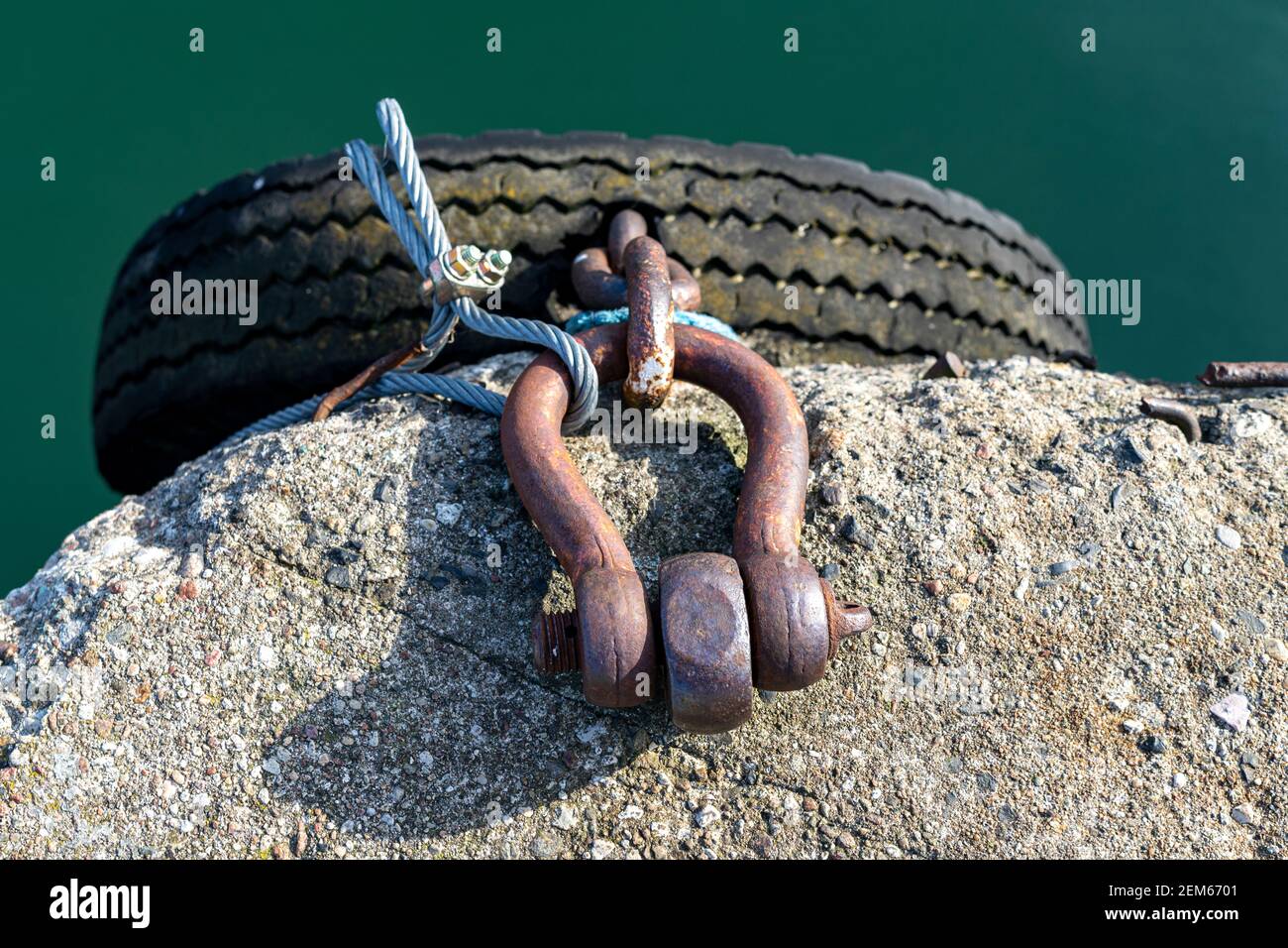 Tire suspended on a shackle in the breakwater. Protection for boats and ships against chafing against concrete quays. Spring season. Stock Photo