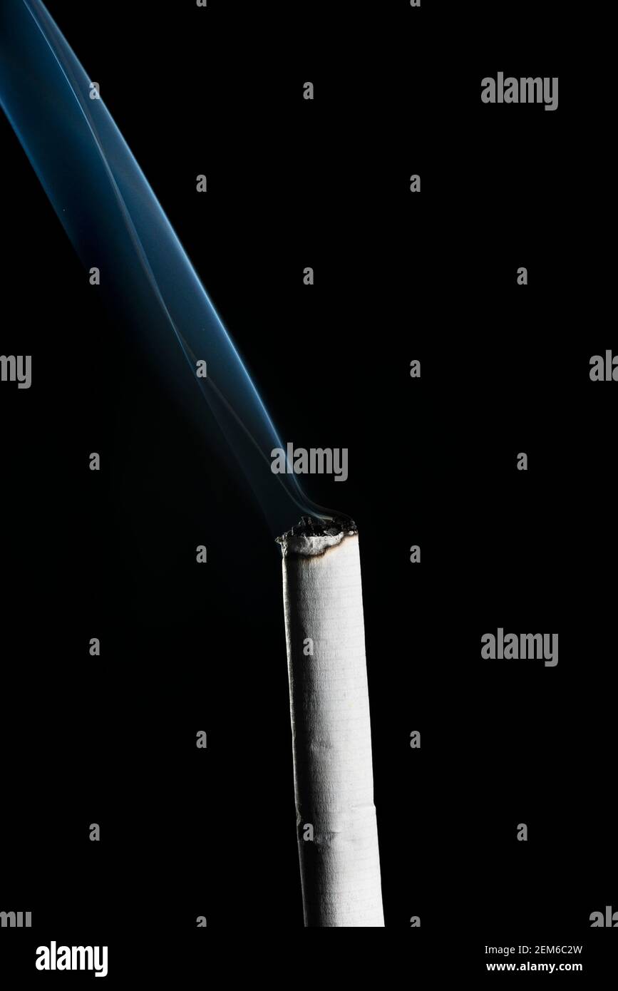 Burning Cigarette with Smoke in a black background. Stock Photo