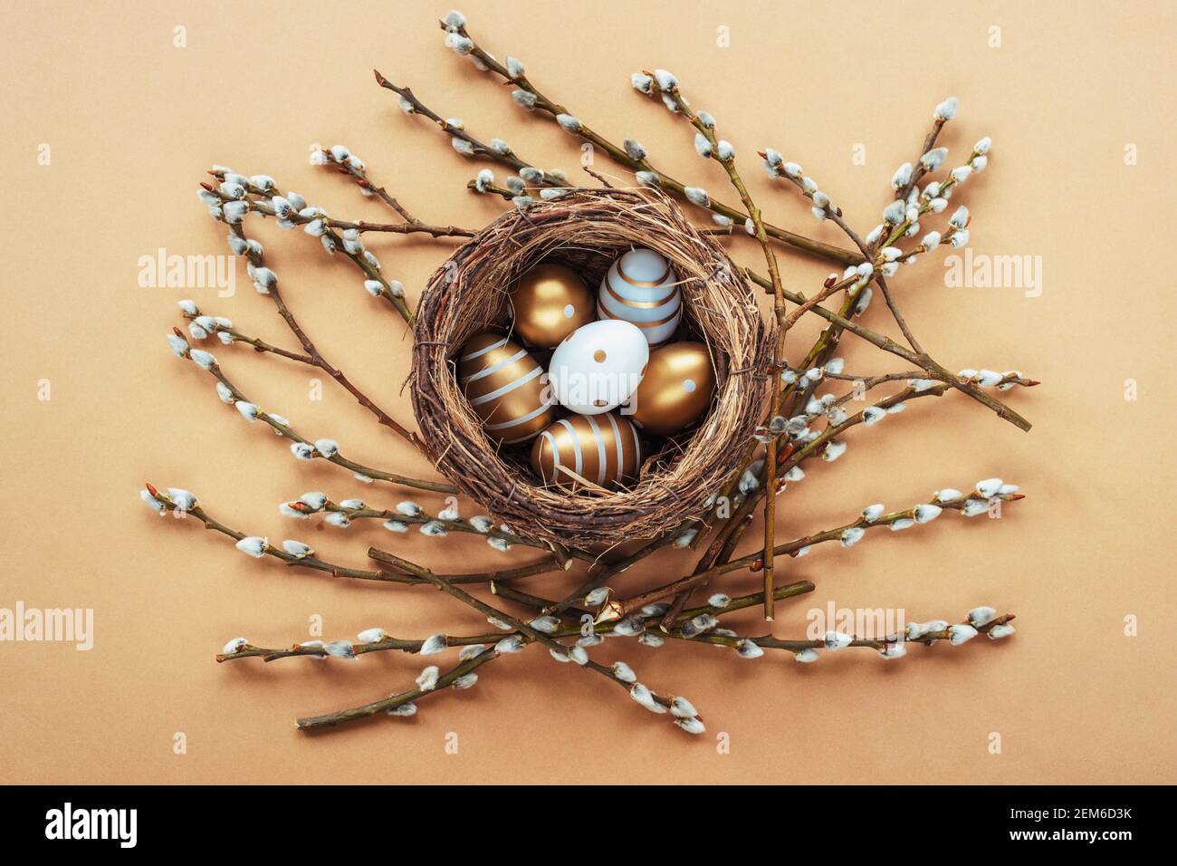 Painted golden and white eggs in the nest with willow twigs on beige ...