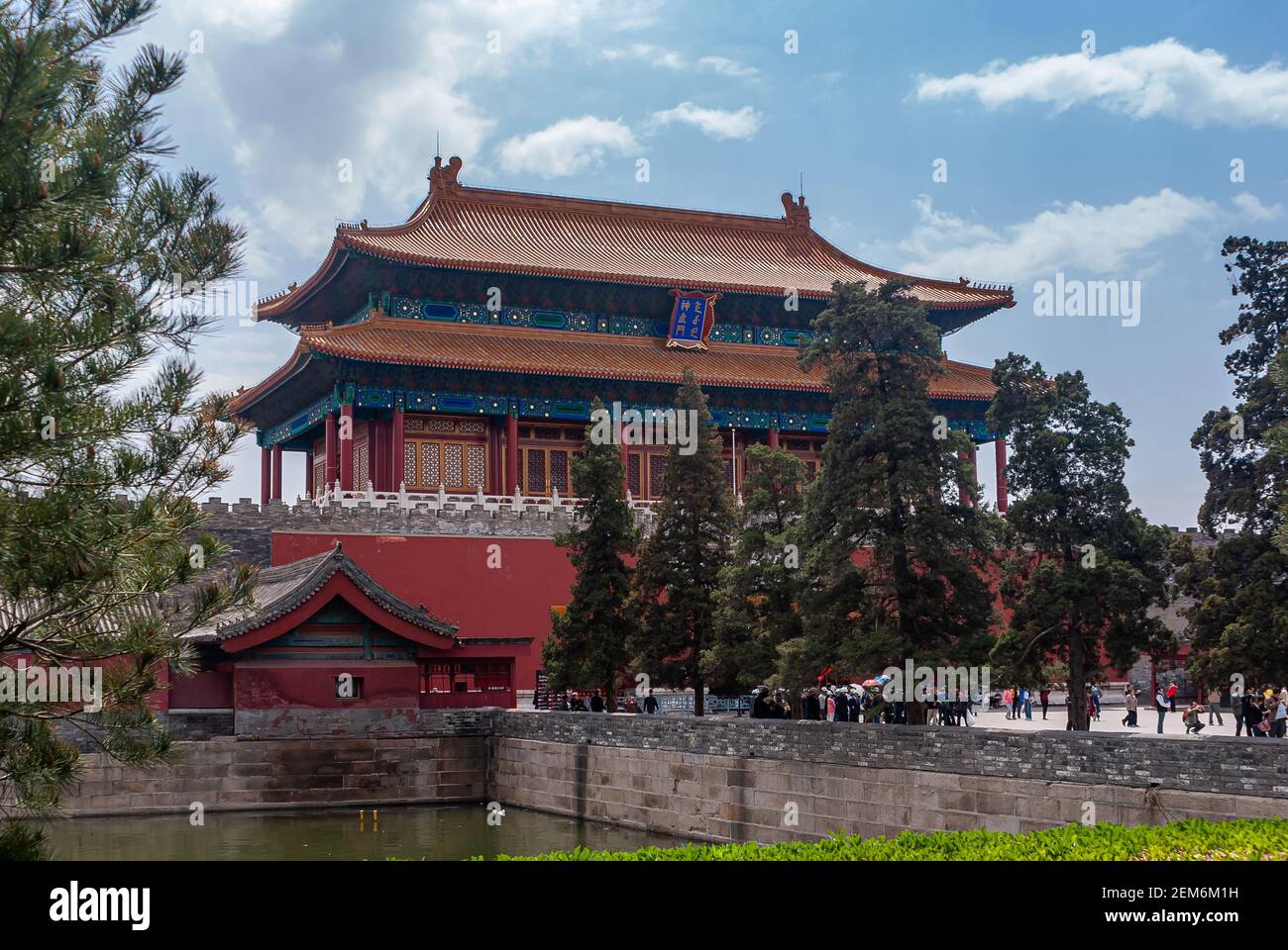 Beijing, China - April 27, 2010: Red Gate of divine Prowess building as exit of Forbidden City North side under blue cloudscape. Moat and green trees. Stock Photo