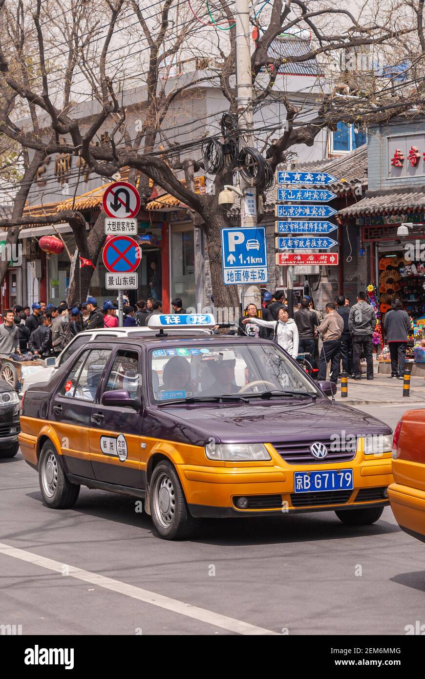 Beijing, China - April 27, 2010: Street scene with purple-orange Volkswagen taxi car stuck in traffic. Sings, stores, and plenty of people. Leaf-less Stock Photo