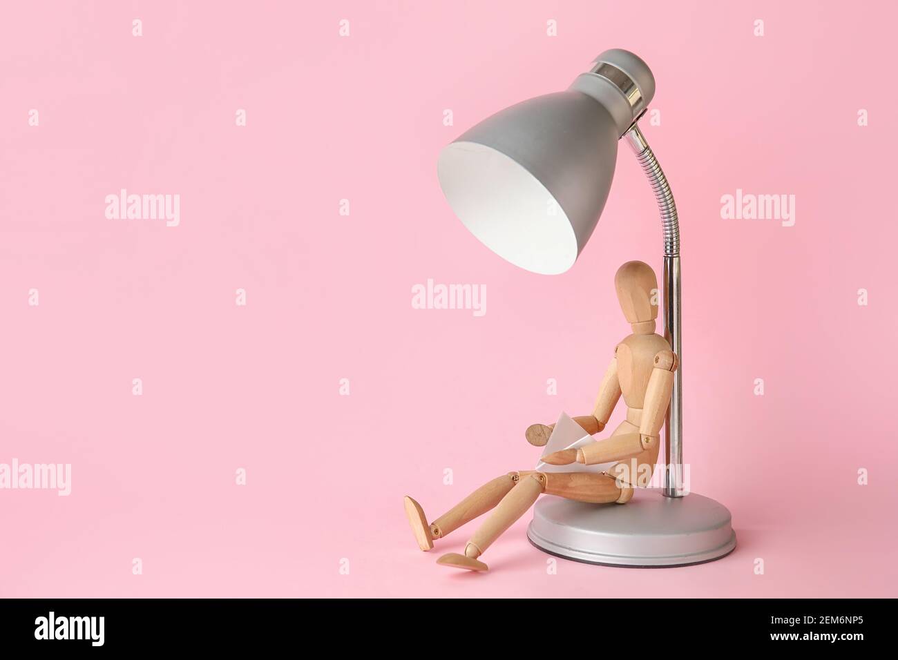 Wooden mannequin with lamp reading book on color background Stock Photo