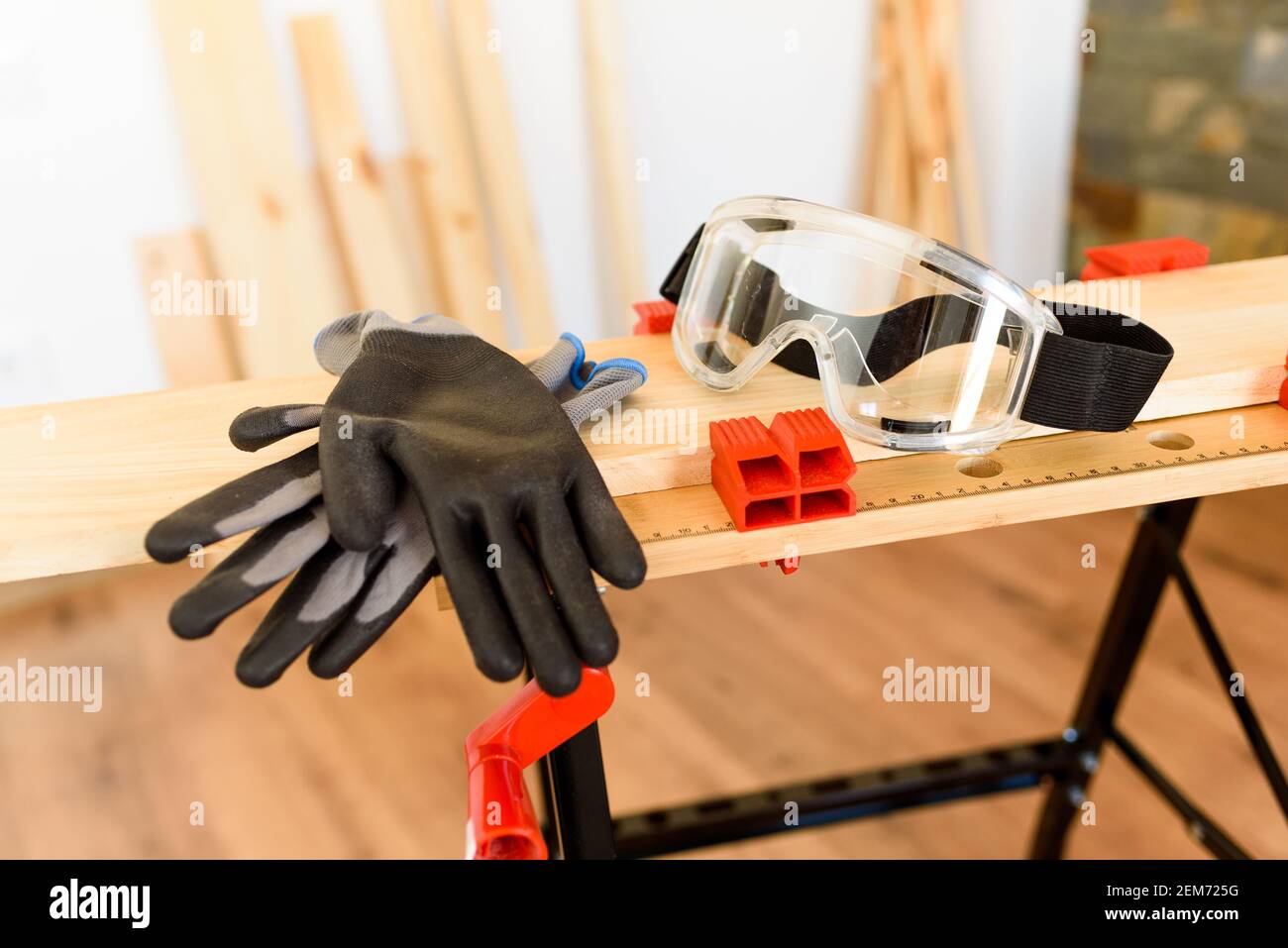 Workbench with protective glasses and safety gloves, without anyone. Inside a flat with wooden floors and white walls. It is daytime and there is natu Stock Photo