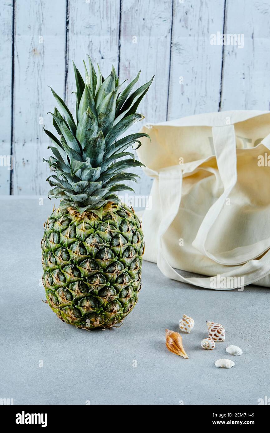 Ripe pineapple and white bag on blue background with seashells Stock Photo