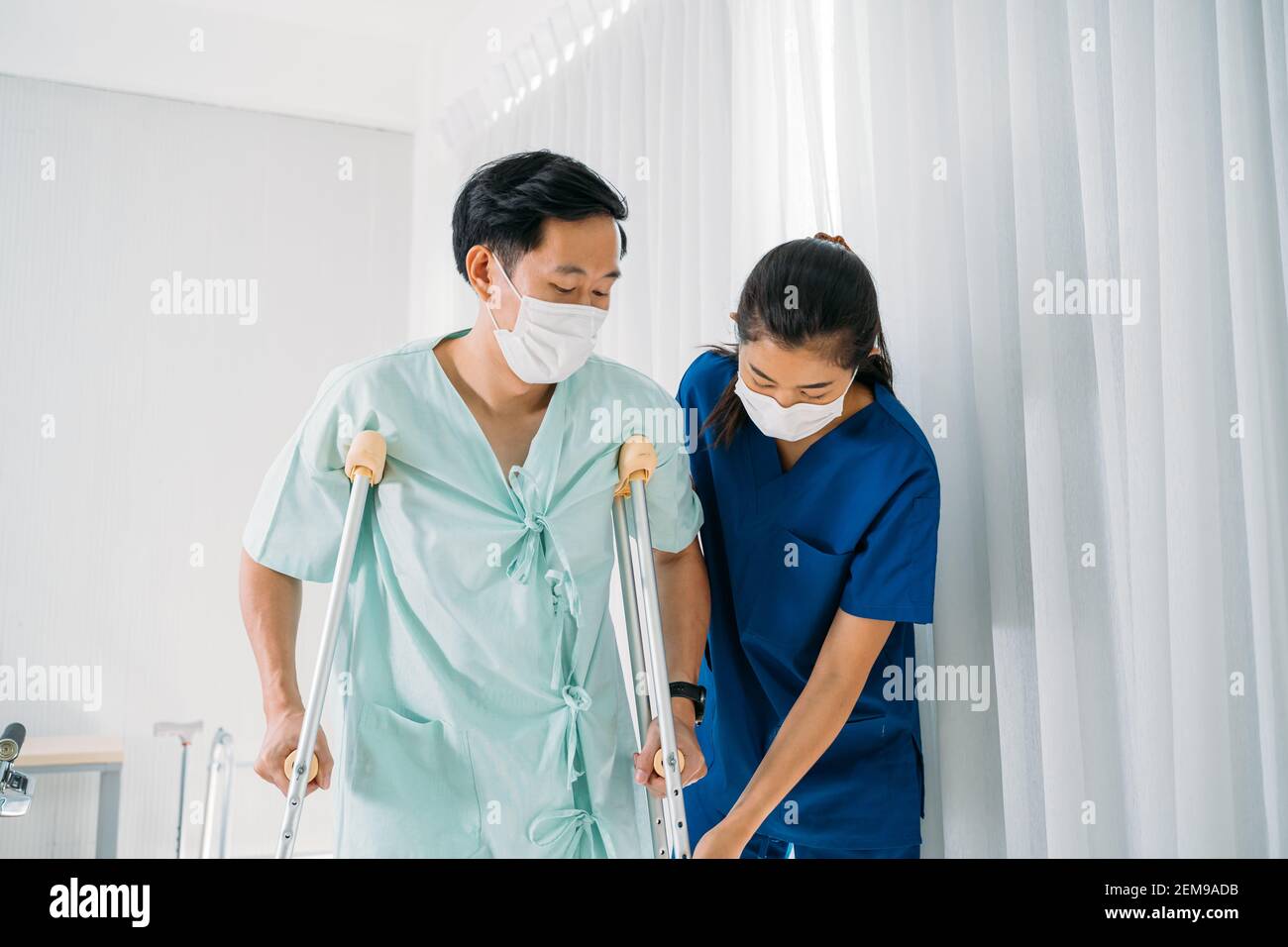 Young female Asian physical therapist in uniform helping man walk using