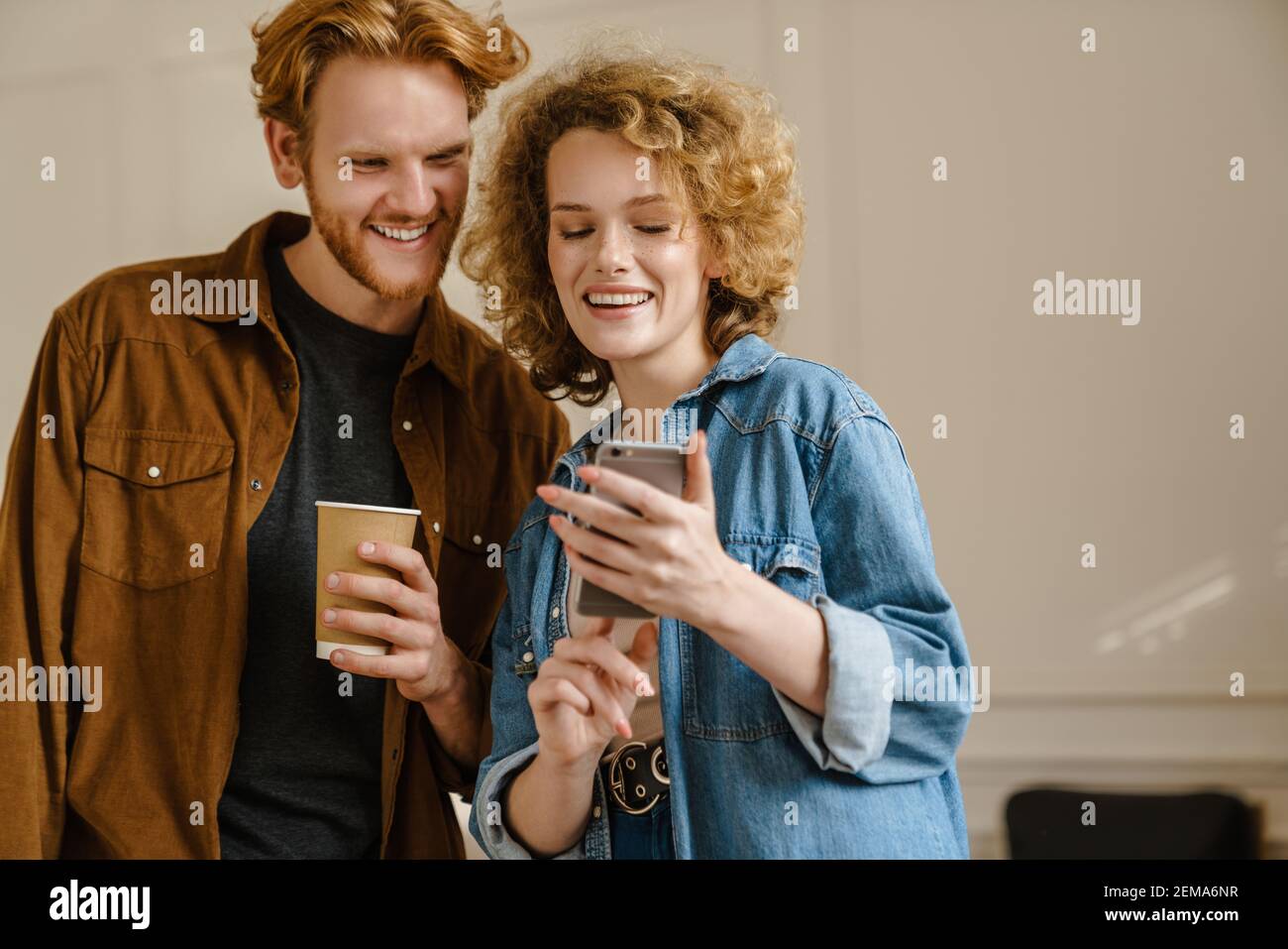 Happy young couple using mobile phones while standing indoors Stock Photo
