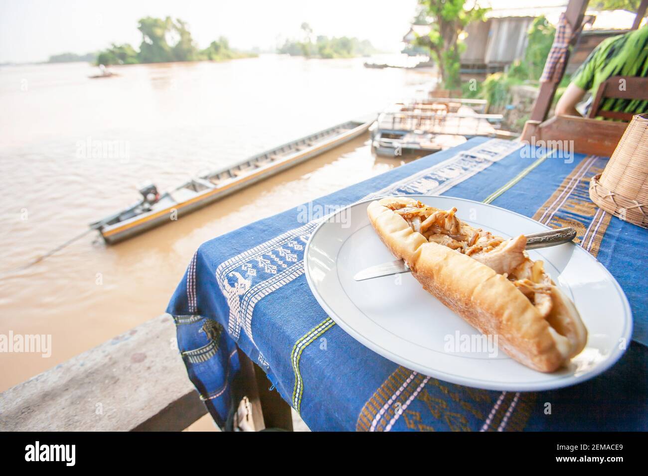 Close-up of Baguette on Laotian traditional tablecloth with scenic view over the Mekong River, a local restaurant in South Laos. Stock Photo