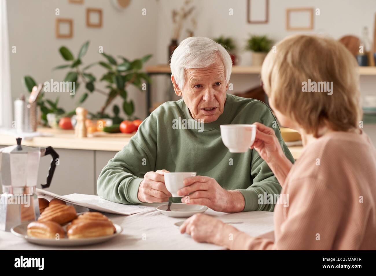 Happy senior couple sitting at the table drinking tea and talking to each other in the kitchen at home Stock Photo