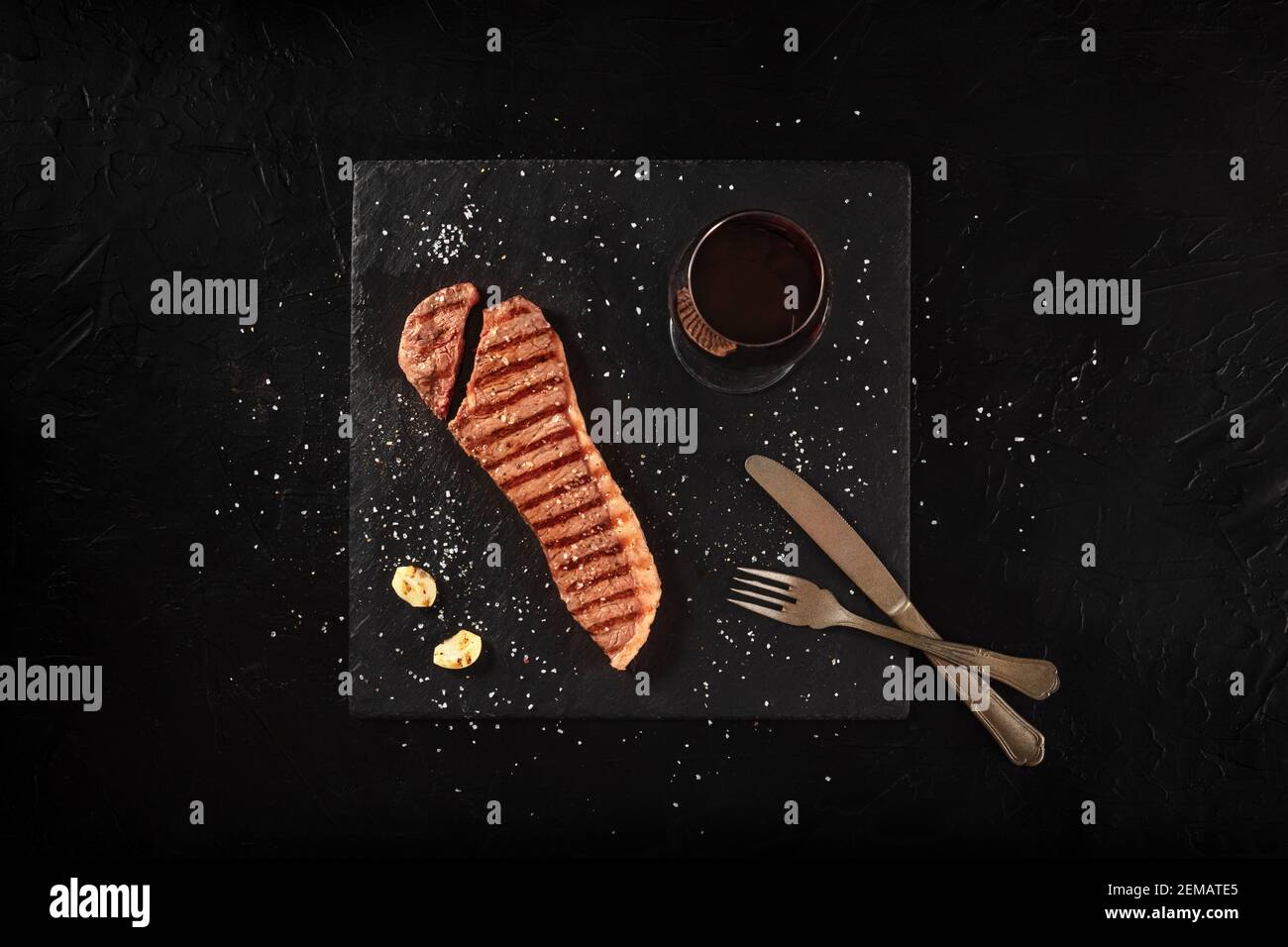 Strip beef steak, cut, shot from the top on a black background, with a glass of wine Stock Photo