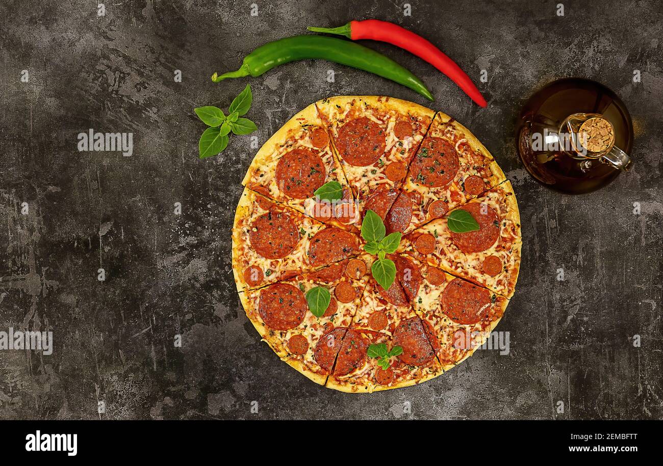 Tasty pepperoni pizza and cooking ingredients, chili, basil on dark background. Stock Photo