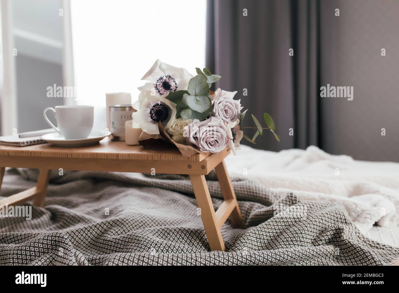 Romantic morning. Wooden coffee table with flowers on bed with plaid,  coffee cup, flowers and candles. Lilac roses with eucalyptus and anemones.  Inter Stock Photo - Alamy, image size:1300x956