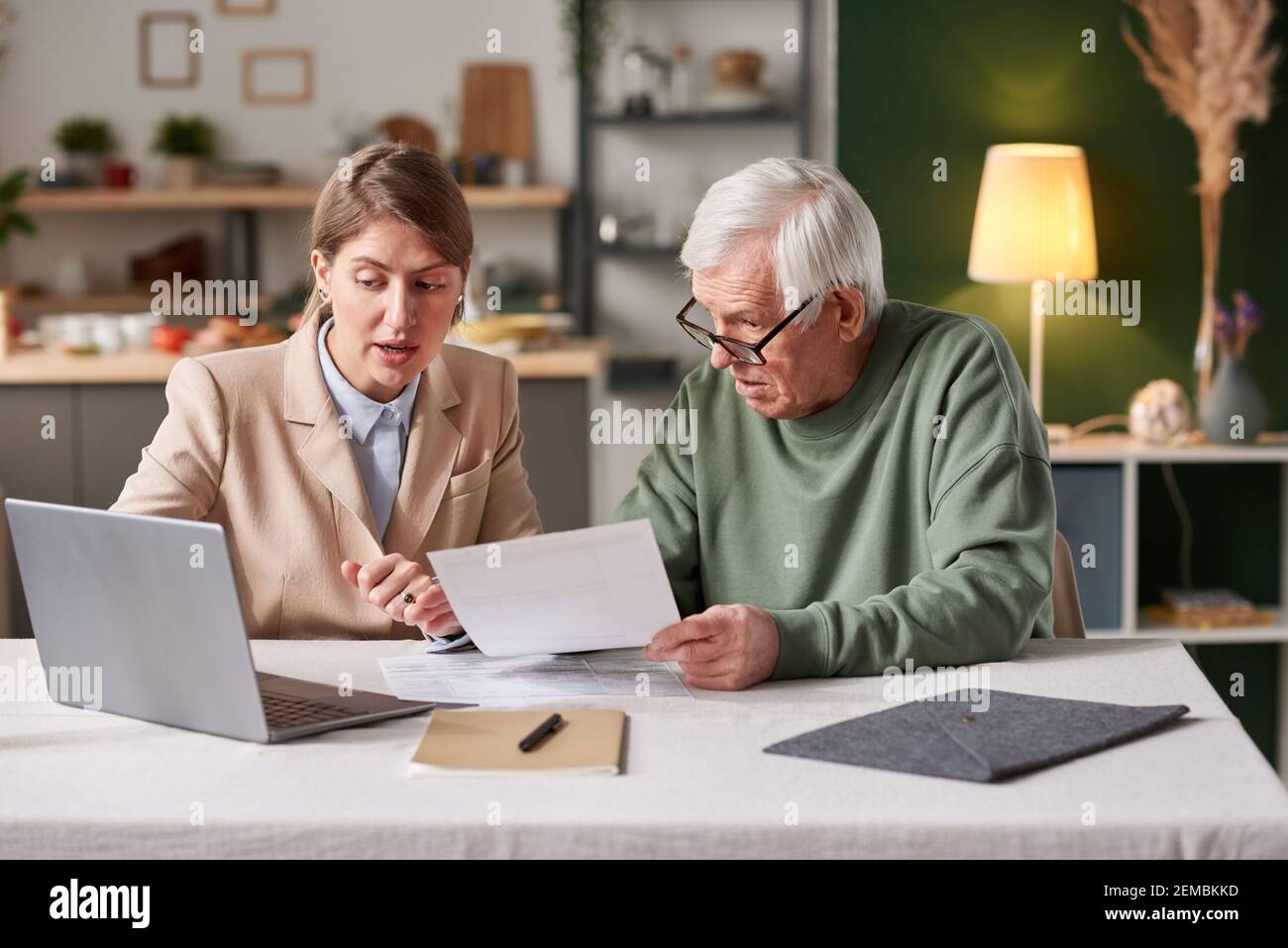 Young businesswoman consulting senior man about financial documents using laptop while they sitting at the table at home Stock Photo