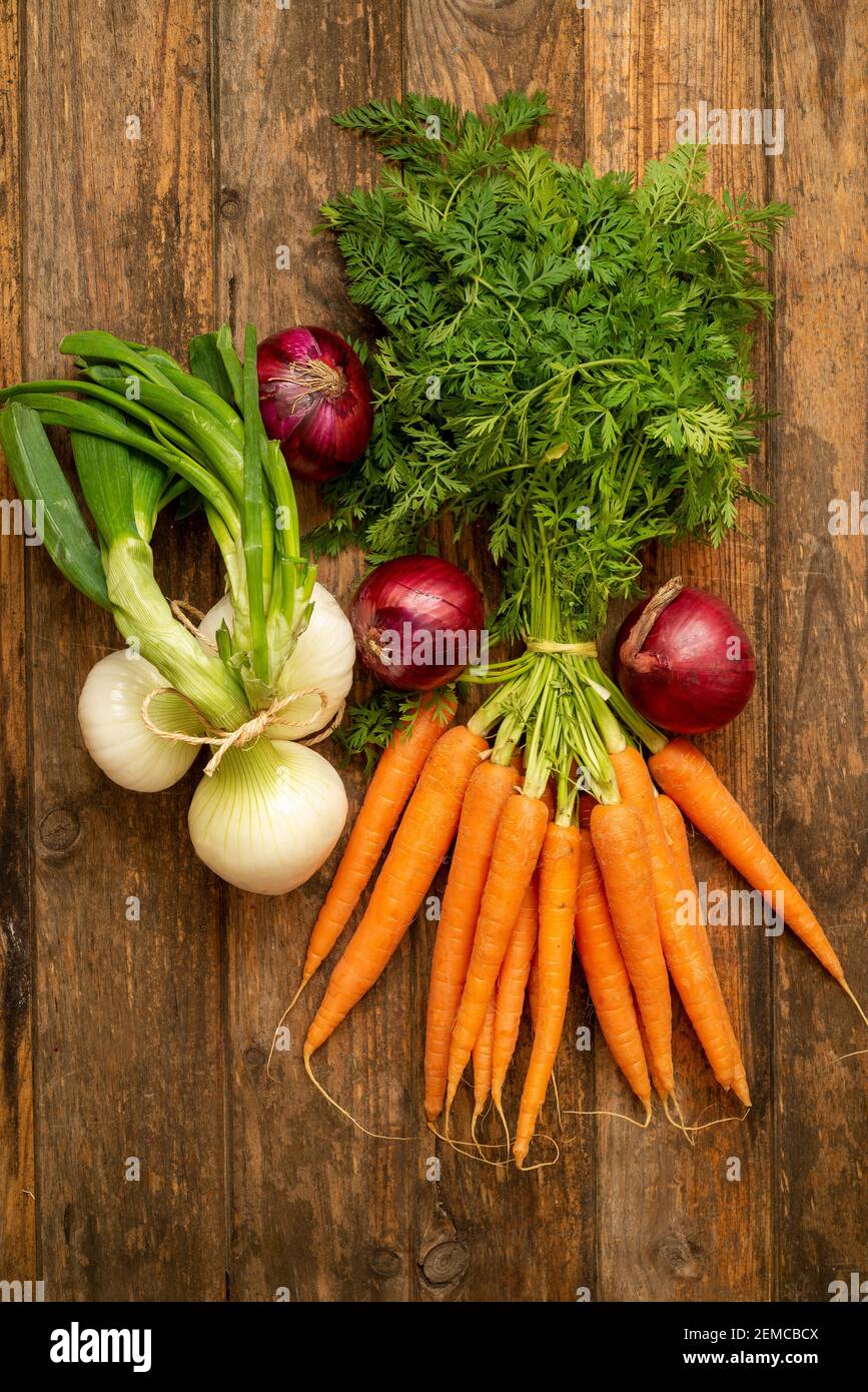 Fresh carrots bunch on rustic wooden background. Red onions and spring onions Stock Photo