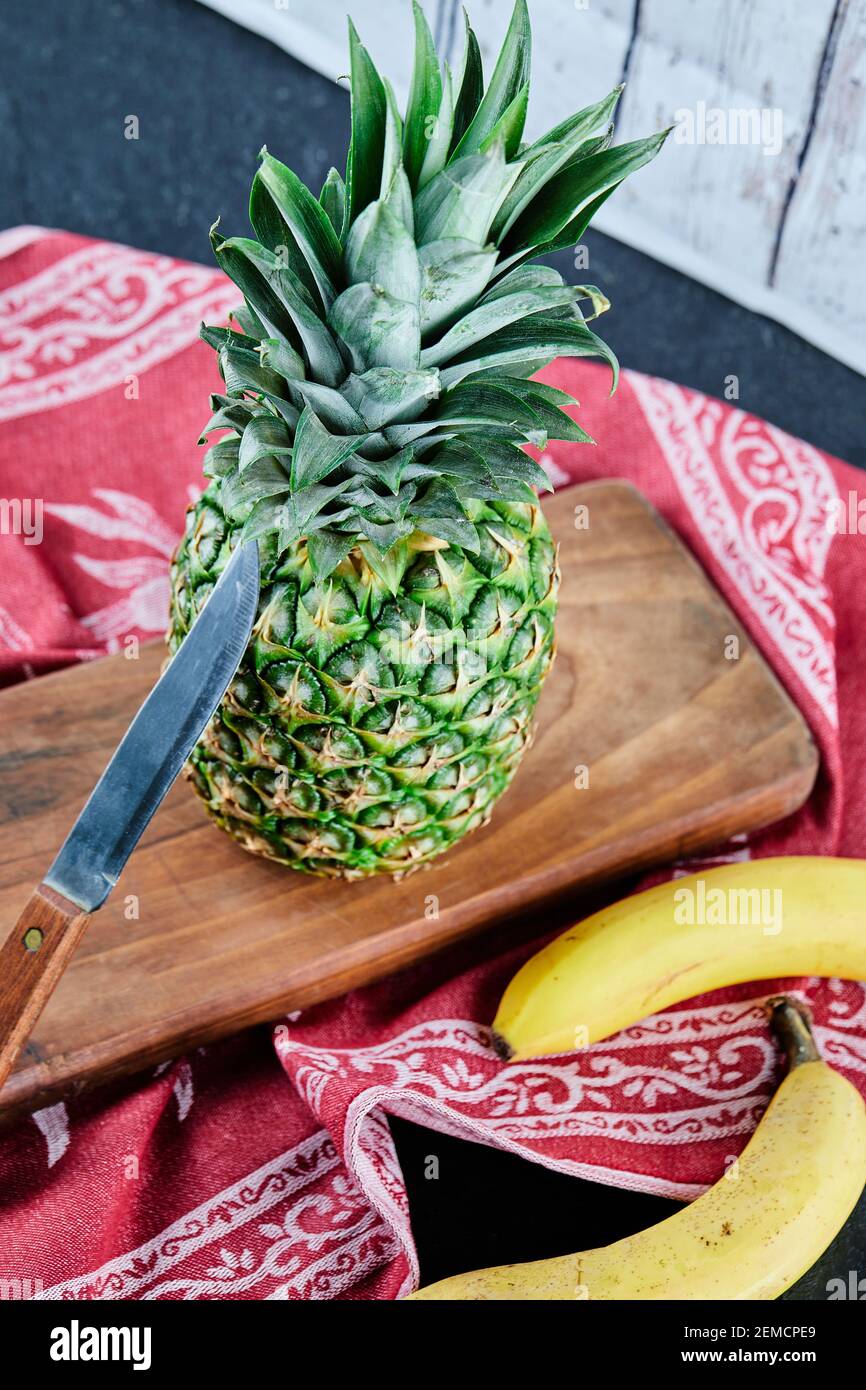 Ripe pineapple and bananas on wooden board with red tablecloth Stock Photo