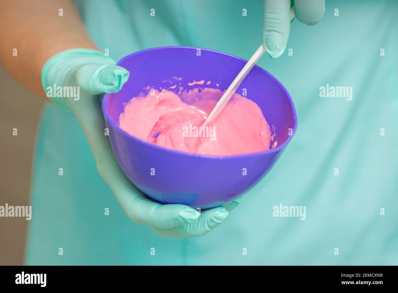 Close up of beautician's hands prepares pink alginate mask mixing in the blue bowl Stock Photo