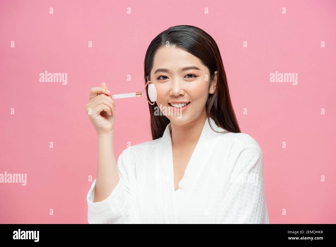 Beautiful young woman with perfect skin using a rose quartz face roller with natural quartz stones Stock Photo