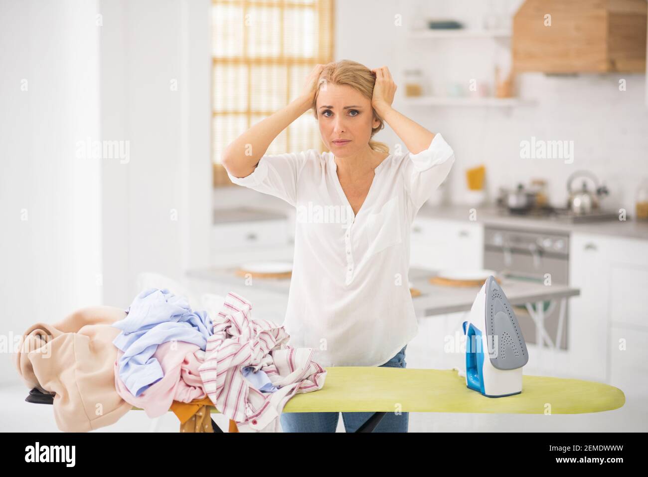 Woman clutching her head with hands in kitchen Stock Photo
