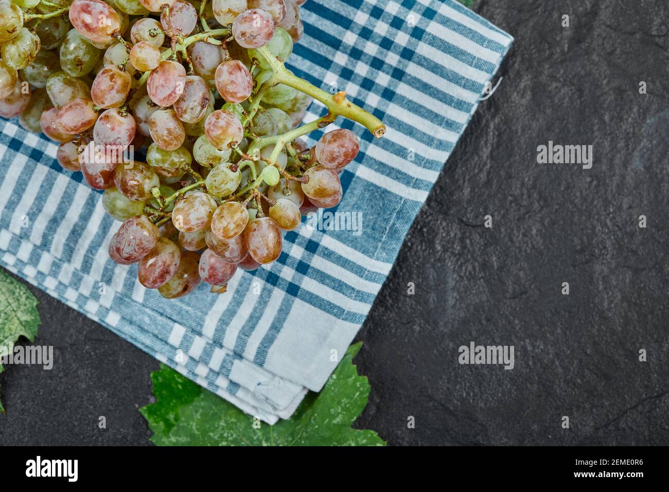 A bunch of red grapes with leaves and blue tablecloth on dark background Stock Photo