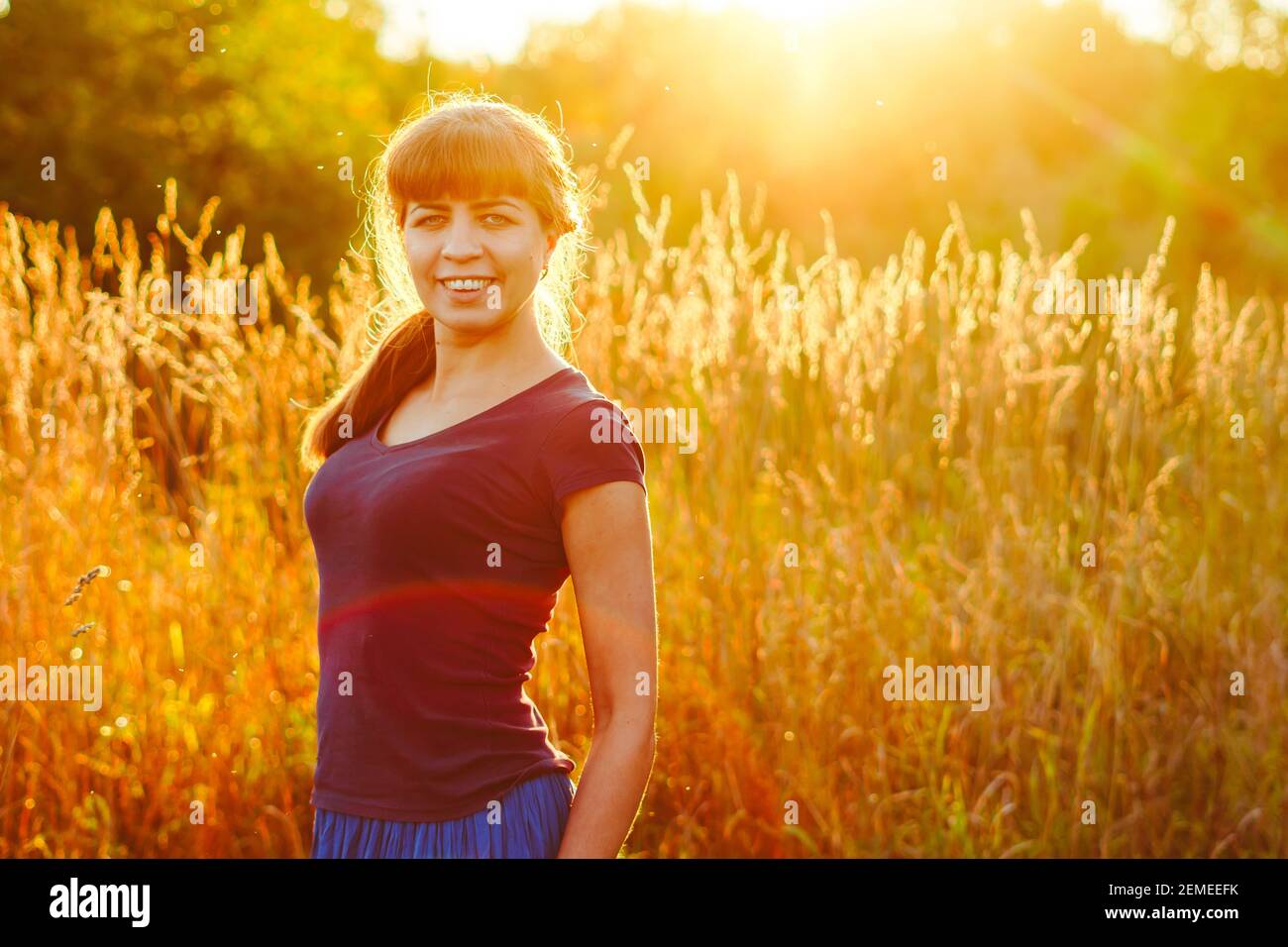 Young woman standing on a wheat field with sunrise on the background ...